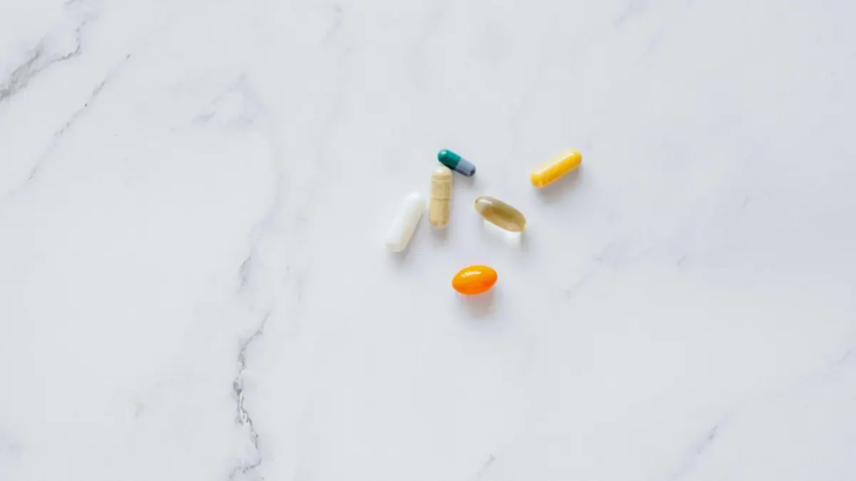 A dog's food bowl next to fresh vegetables and a bottle of vitamin capsules on a kitchen counter